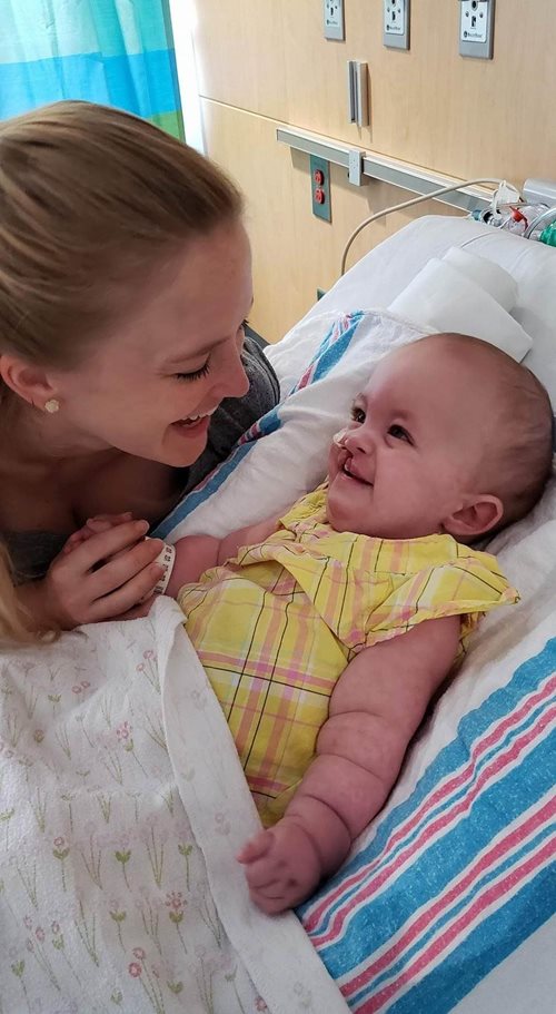 Heidi sonriendo y sosteniendo la mano de su madre en la cama del hospital