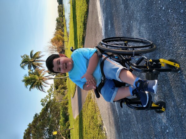 Nicolas smiles sitting in a wheelchair on a sunny day
