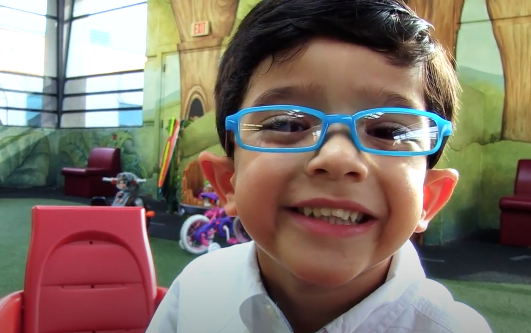 Ralphie smiling, wearing blue glasses while playing in the Hospital playroom.