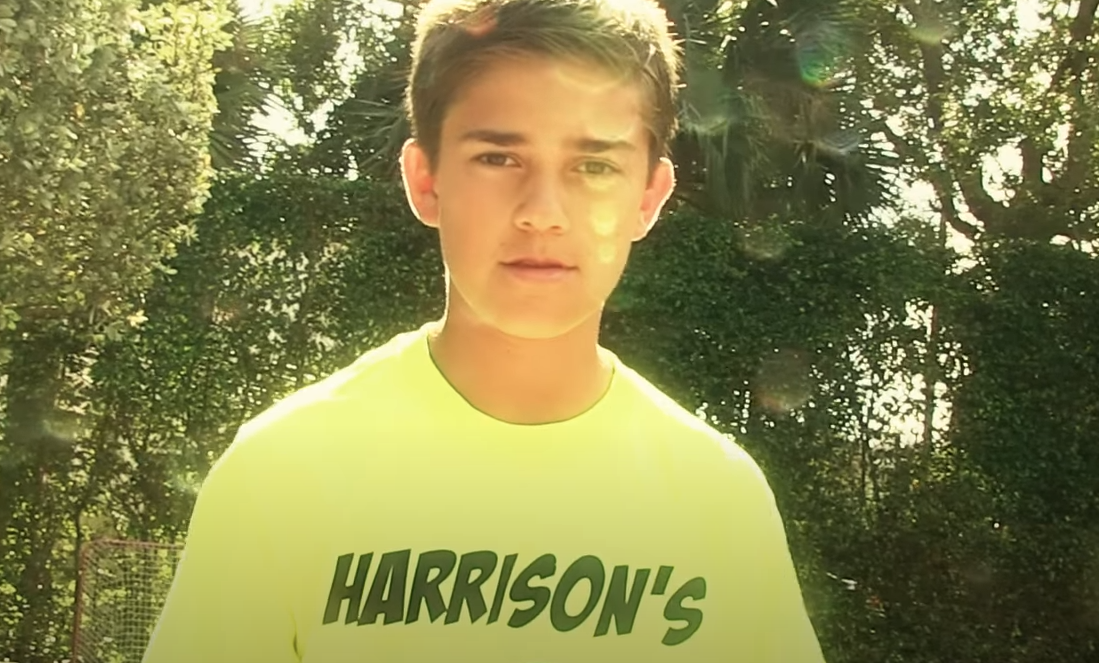 Harrison wearing a lime colored T-shirt, standing in front of trees. 