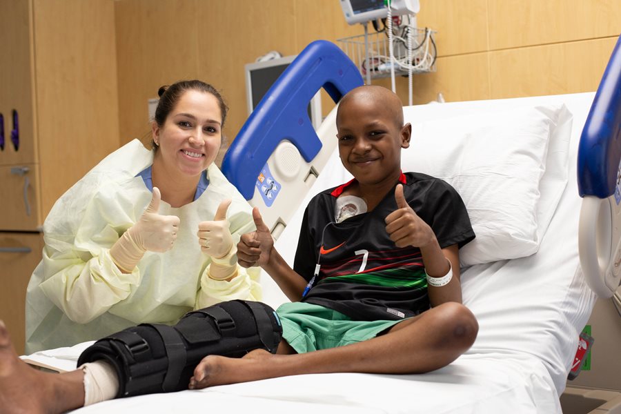 Tyler on a hospital bed giving two thumbs up next to a female clinician. 