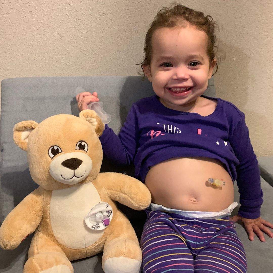 Zuri, next to a stuffed bear with an abdominal feeding tube just like hers. 