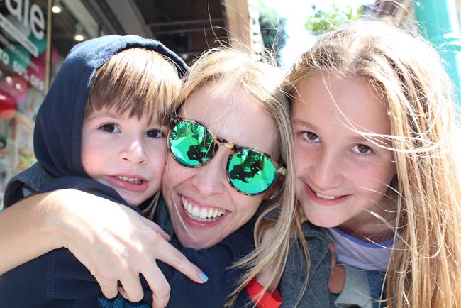 A mother wearing reflective sunglasses, surrounded by her two young children 