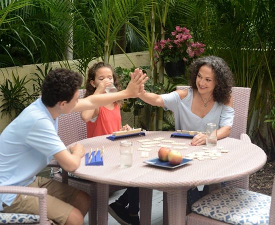 A family plays a board game at a backyard patio table
