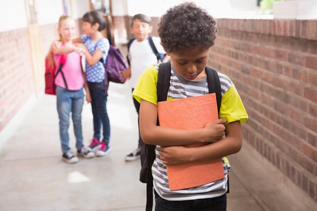 A young boy walks with his head down as children laugh mockingly in the distance