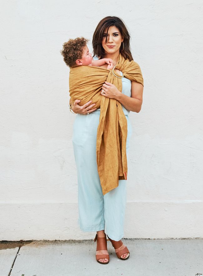 A Mother holding her son in a soft wrapping that wraps around her shoulder, close to her chest