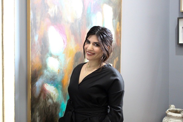 A women in a black dress standing in front of color artwork