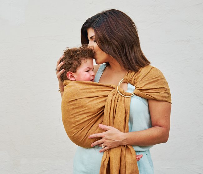 A Mother holding her son in a soft wrapping that wraps around her shoulder, close to her chest