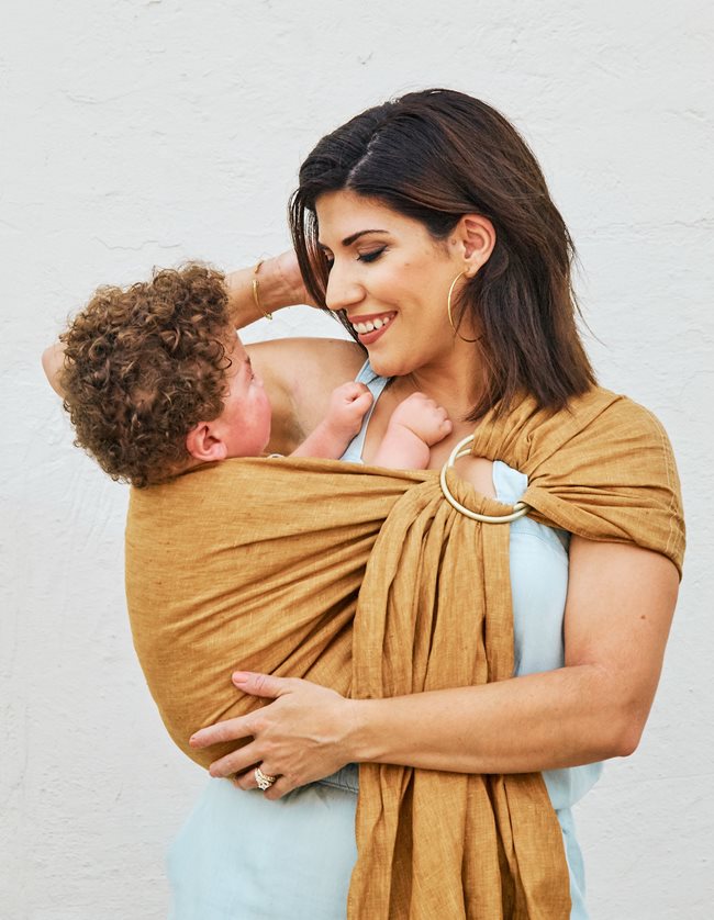 A Mother holding her son in a soft wrapping that wraps around her shoulder, close to her chest