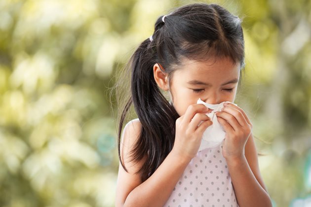 A young girl blows her nose in a tissue