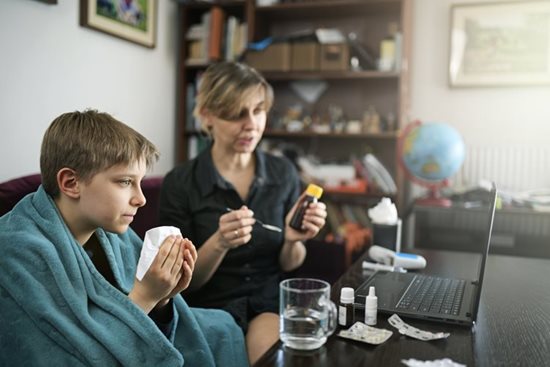 A mother taking care of her ill son while they both sit on a couch