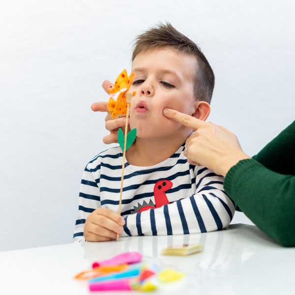 A young boy blows into a tiny windmill while his mother playfully pokes his cheeks