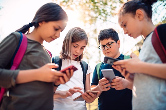Grupo de 4 jóvenes, 4 niñas y 1 niño usando las redes sociales en sus celulares.