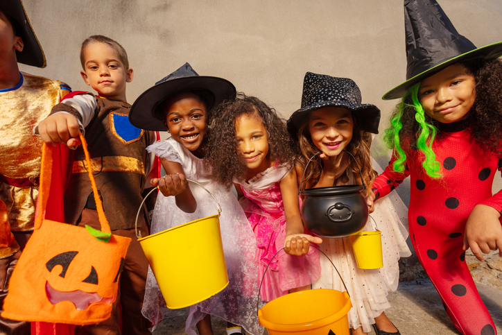 kids of different backgrounds in costumes holding baskets for halloween candy