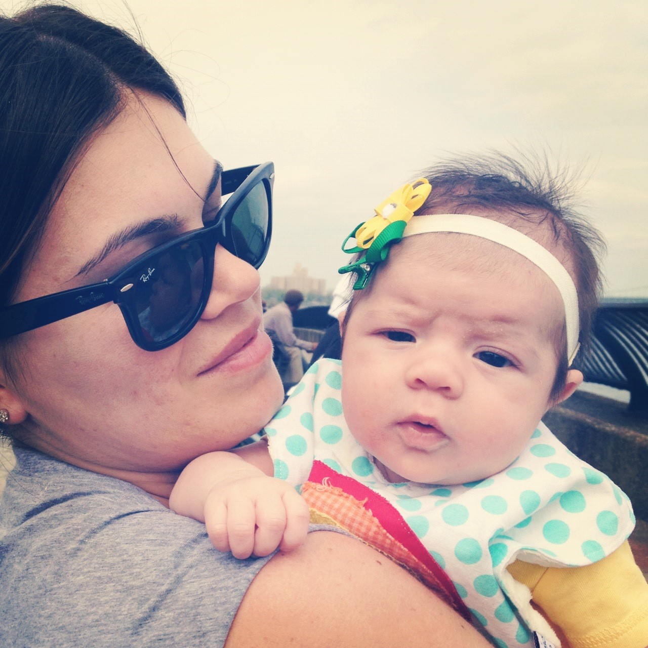 A mother wearing sun glasses holding her young infant 