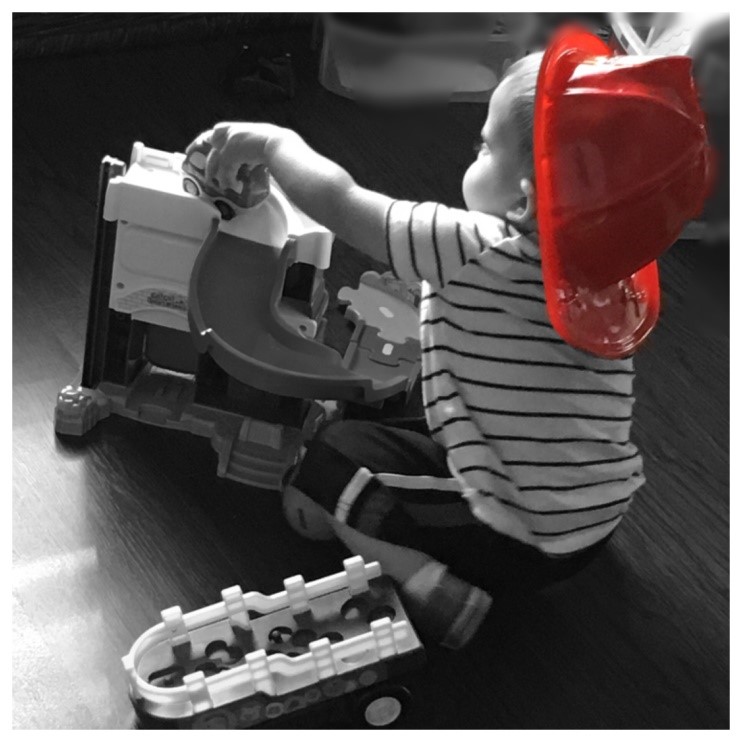 A little boy playing with toys in a fire fighter hat