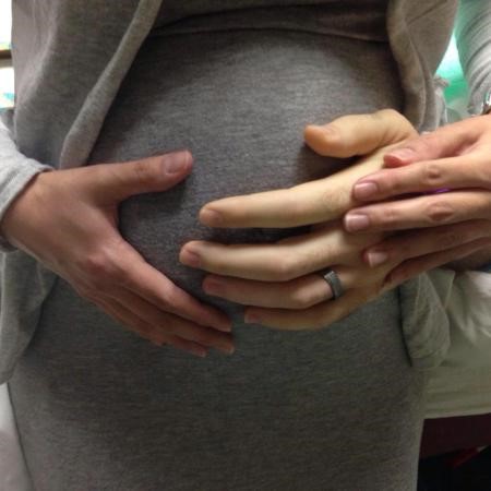 A pregnant belly being held by a mother and father's hands. 