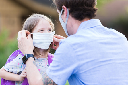 A mask wearing father placing a mask onto a his daughter 