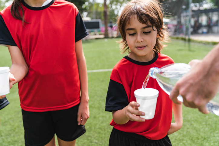 Young soccer players holding a cup as a coach pours water