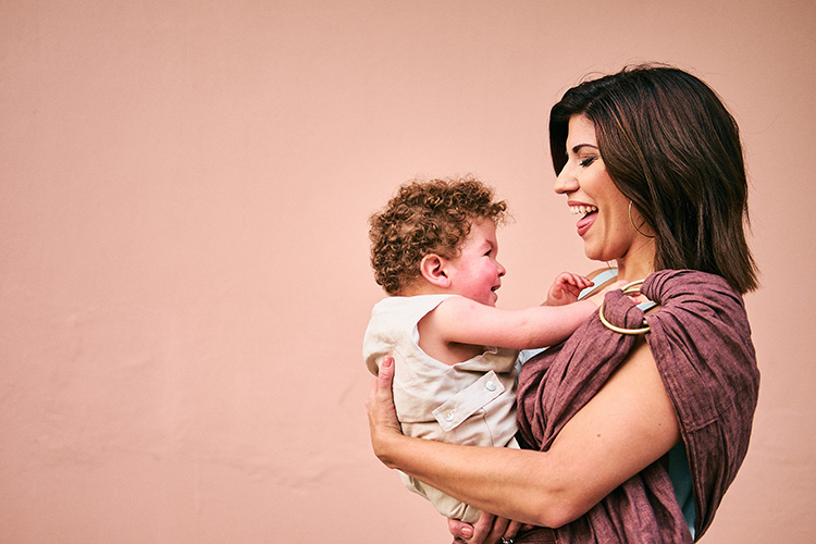 A smiling mother holding her young son in front of a pink wall