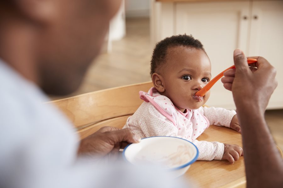 A baby in fed baby food on a spoon by their father 