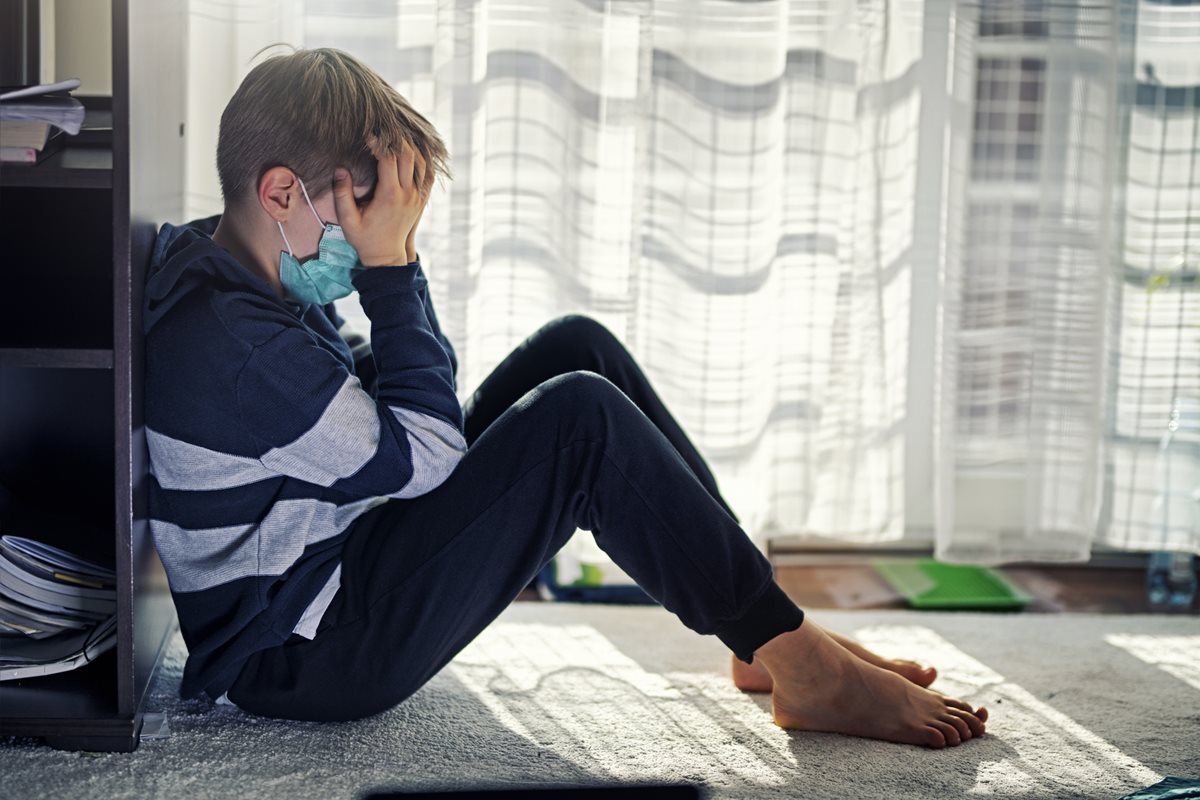 A stressed child wearing a mask holding is head 