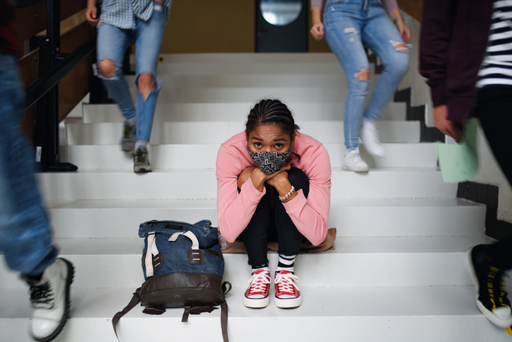 A scared student sitting on steps while students pass er