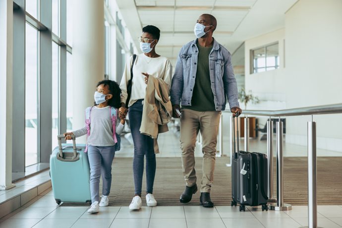 family with facemasks walking down airport hallway.