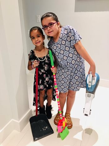 Two young children smiling while holding a dust pan and broom