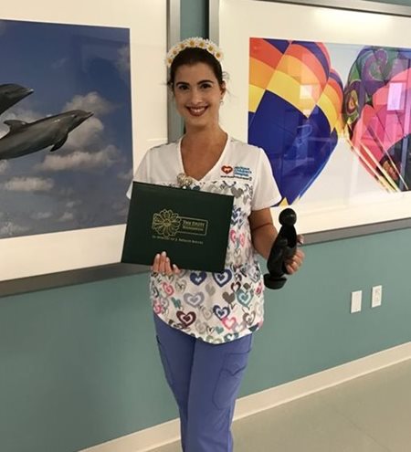 awardee wearing a headband of daisies, daisy award statue, and certificate.