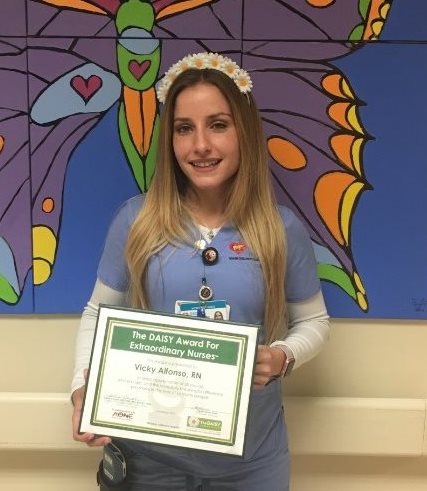 awardee wearing a headband of daisies, daisy award statue, and certificate.