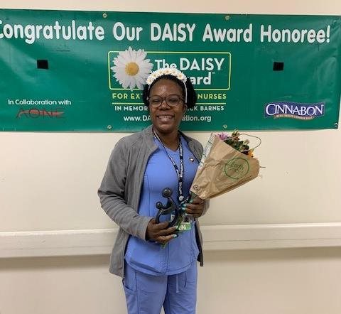 awardee wearing a headband of daisies, daisy award statue, and certificate.