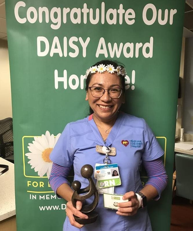 awardee wearing a headband of daisies, daisy award statue, and certificate.