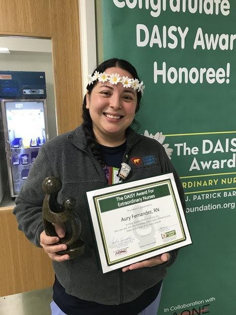 awardee wearing a headband of daisies, daisy award statue, and certificate.