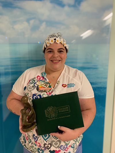 awardee wearing a headband of daisies, daisy award statue, and certificate.