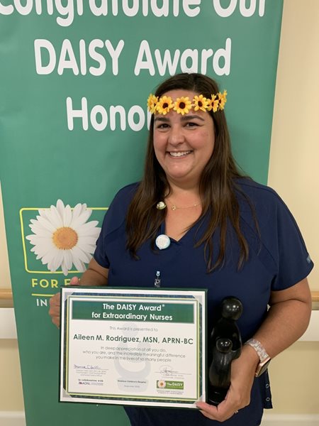 awardee wearing a headband of daisies, daisy award statue, and certificate.