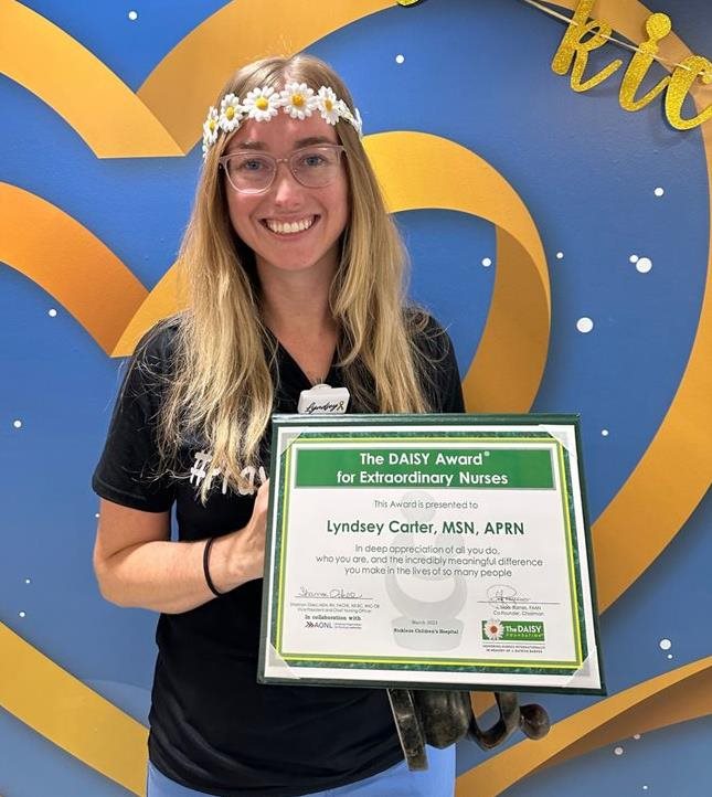 awardee wearing a headband of daisies, daisy award statue, and certificate.