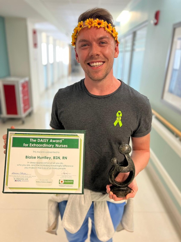 awardee wearing a headband of daisies, daisy award statue, and certificate.