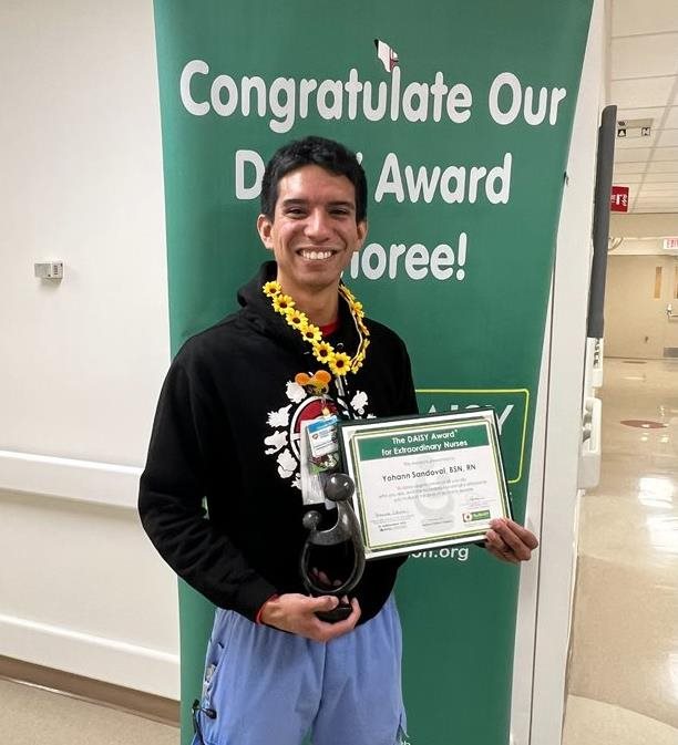 awardee wearing a headband of daisies, daisy award statue, and certificate.