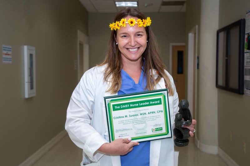 awardee wearing a headband of daisies, daisy award statue, and certificate.