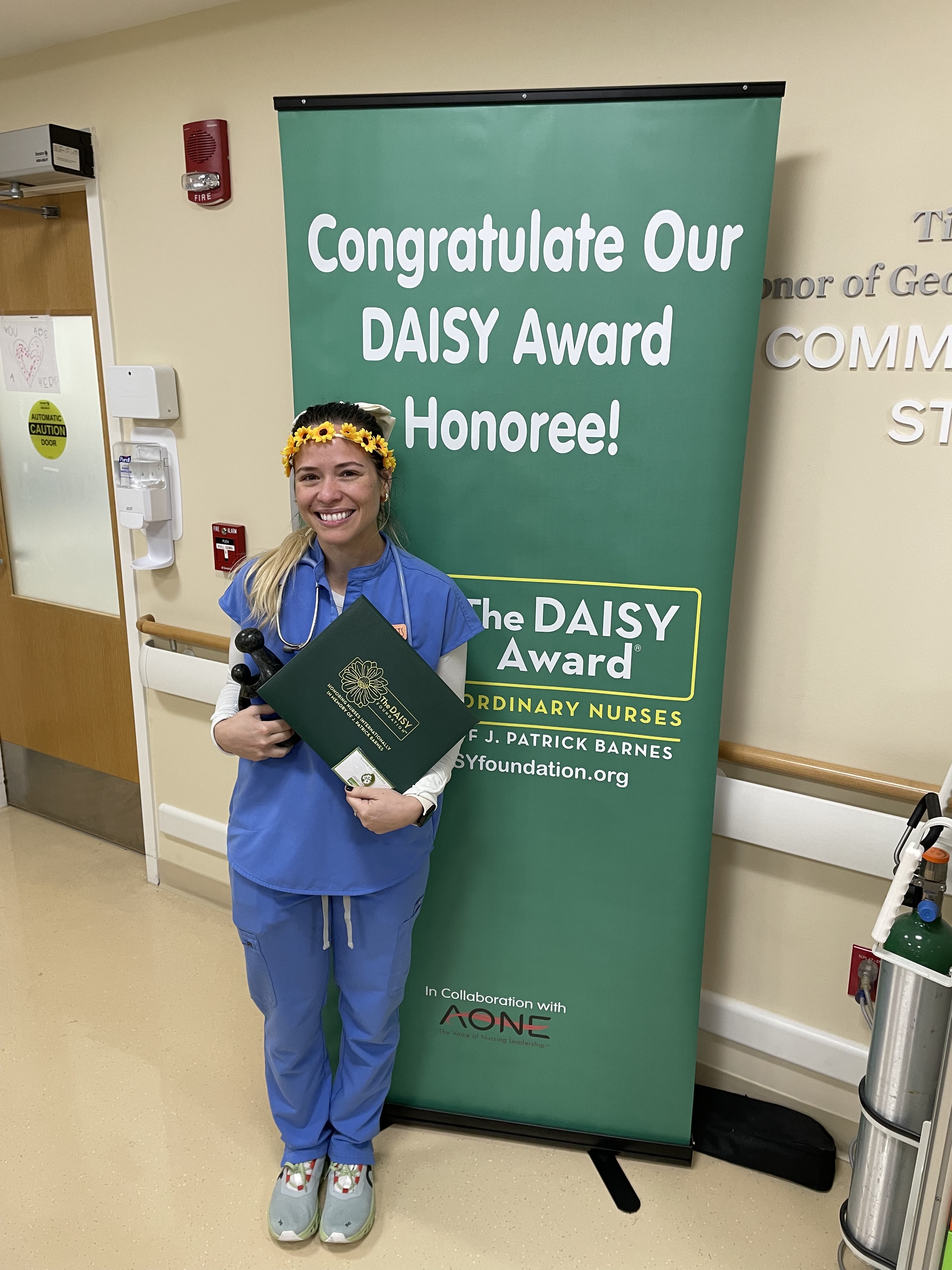 awardee wearing a headband of daisies, daisy award statue, and certificate.