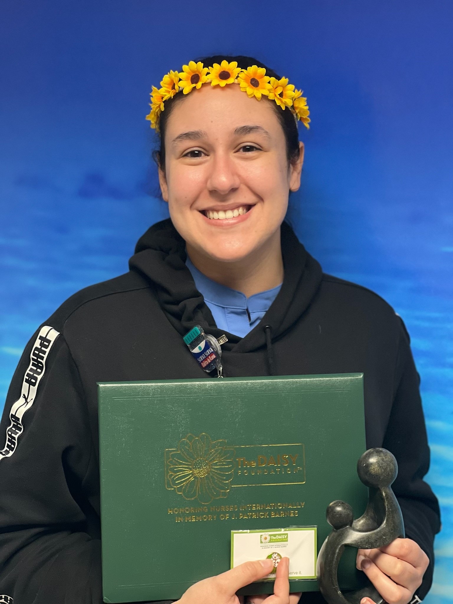 awardee wearing a headband of daisies, daisy award statue, and certificate.