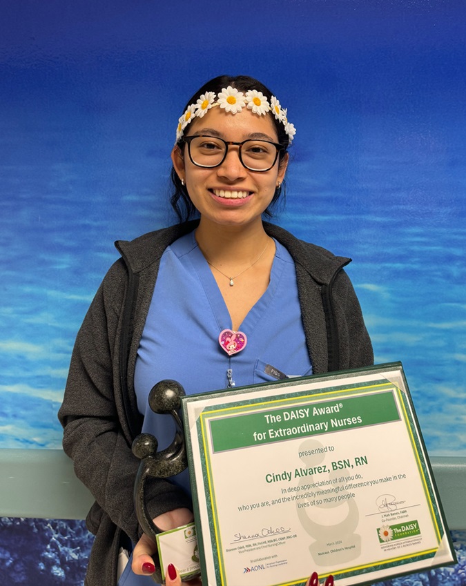 awardee wearing a headband of daisies, daisy award statue, and certificate.