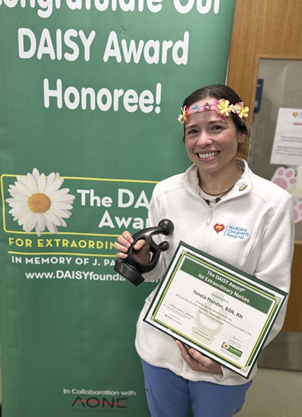 awardee wearing a headband of daisies, daisy award statue, and certificate.