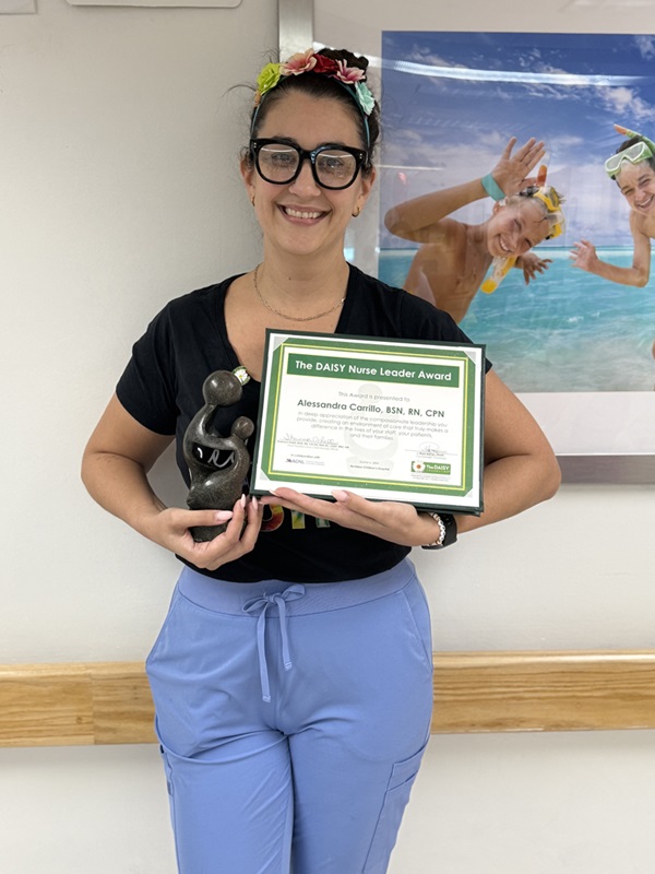 awardee wearing a headband of daisies, daisy award statue, and certificate.