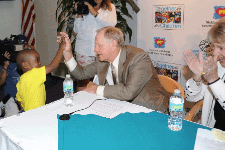 Jack Nicklaus sitting in a table giving a high five to a little boy during a press conference.