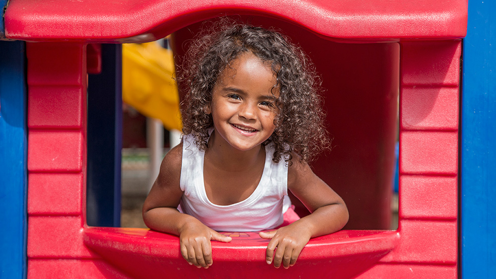 curly haired girl happily leaning out of playhouse