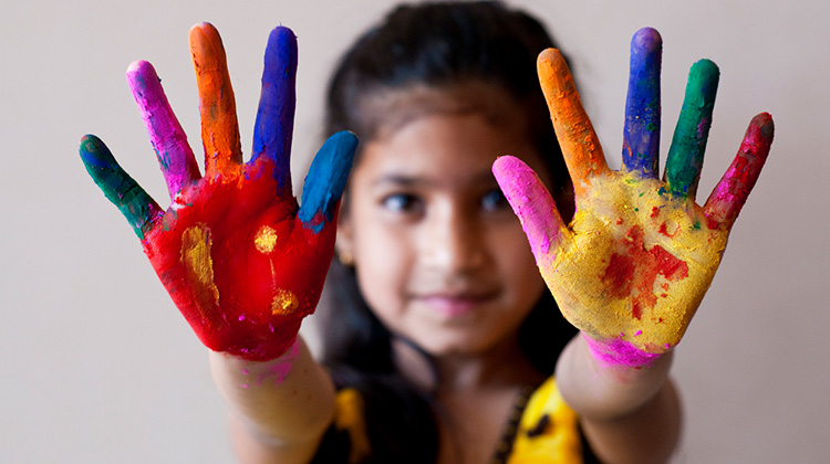 niña con las manos extendidas con pintura en sus dedos y palmas