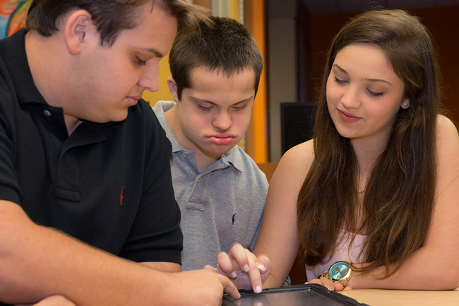 two siblings looking at a tablet with their special needs brother.
