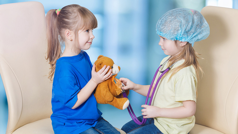 dos niñas jugando al doctor con un osito